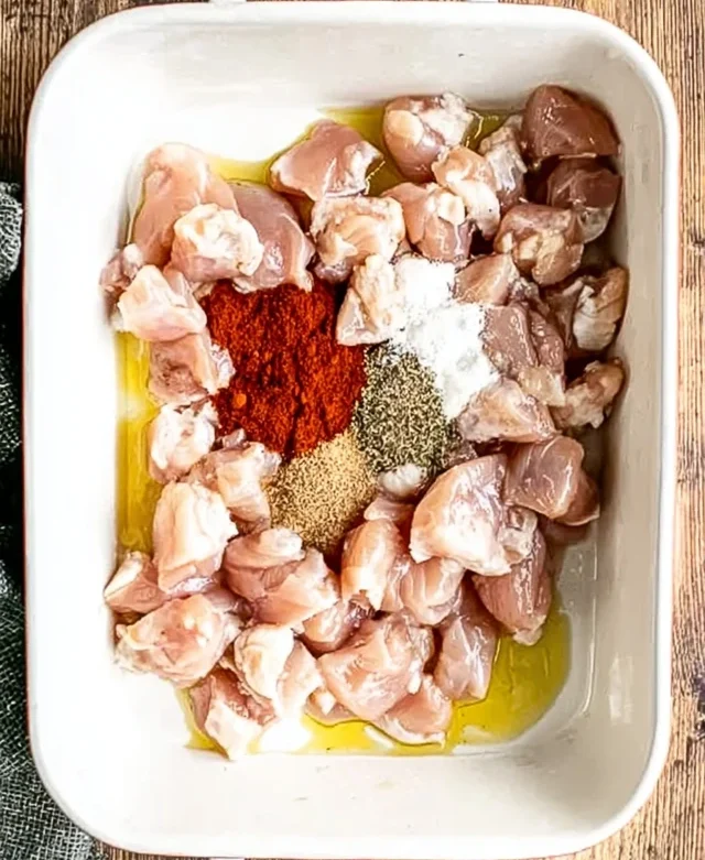 Raw chicken pieces mixed with oil and spices in a baking dish
