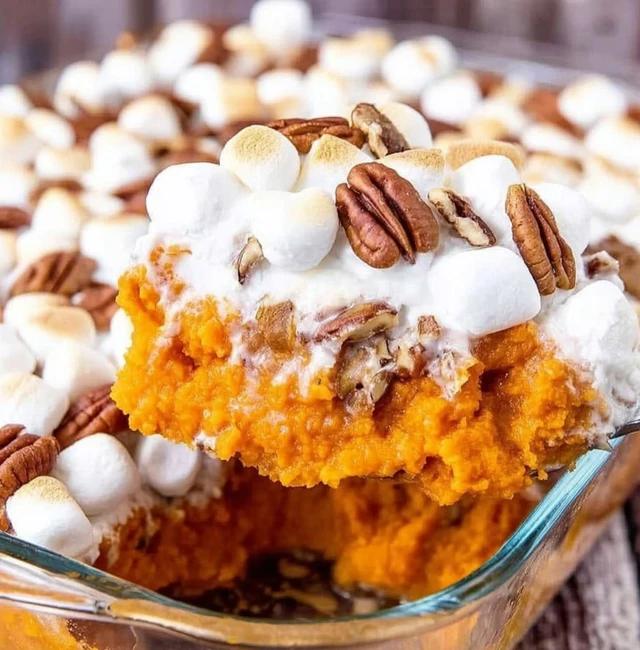 Sweet potato casserole lifted from a glass baking dish with toasted marshmallows and pecans, showing creamy orange filling and fluffy topping