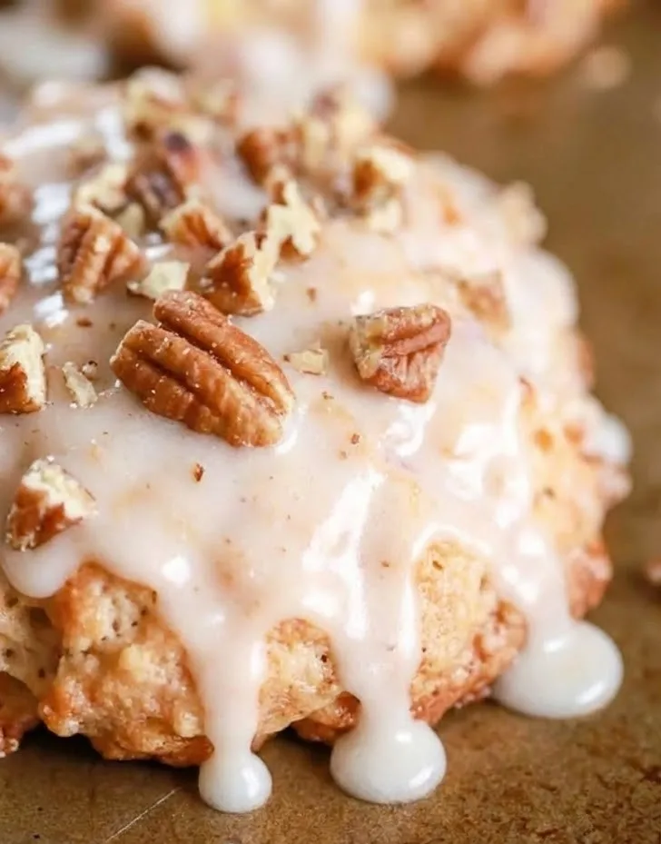 Close-up of baked apple fritter drizzled with vanilla glaze and topped with chopped pecans, showing moist crumb and glossy icing