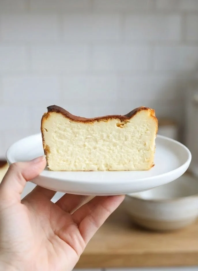 Hand holding a slice of Basque cheesecake from a loaf pan on a white plate