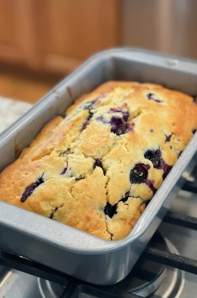 Freshly baked blueberry cream cheese loaf in a loaf pan with golden top and bursting blueberries