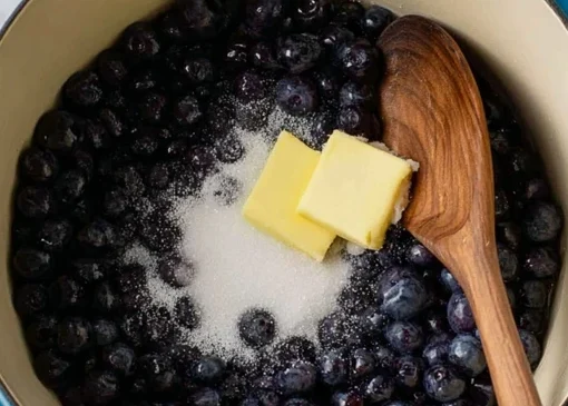 Preparing blueberry filling for blueberry crumb bars with fresh blueberries, sugar, and butter in a pot