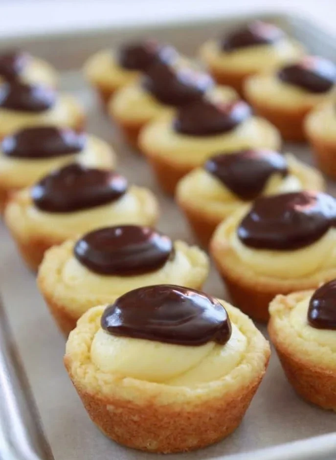 Boston cream pie cookies with vanilla cream and chocolate topping arranged on a baking sheet