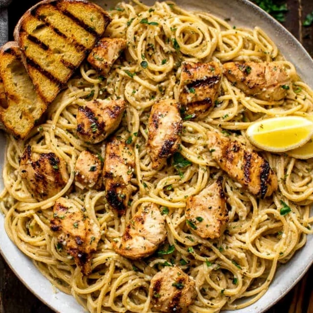Cowboy butter chicken pasta in a skillet with creamy garlic sauce, grilled chicken, lemon, and toasted bread