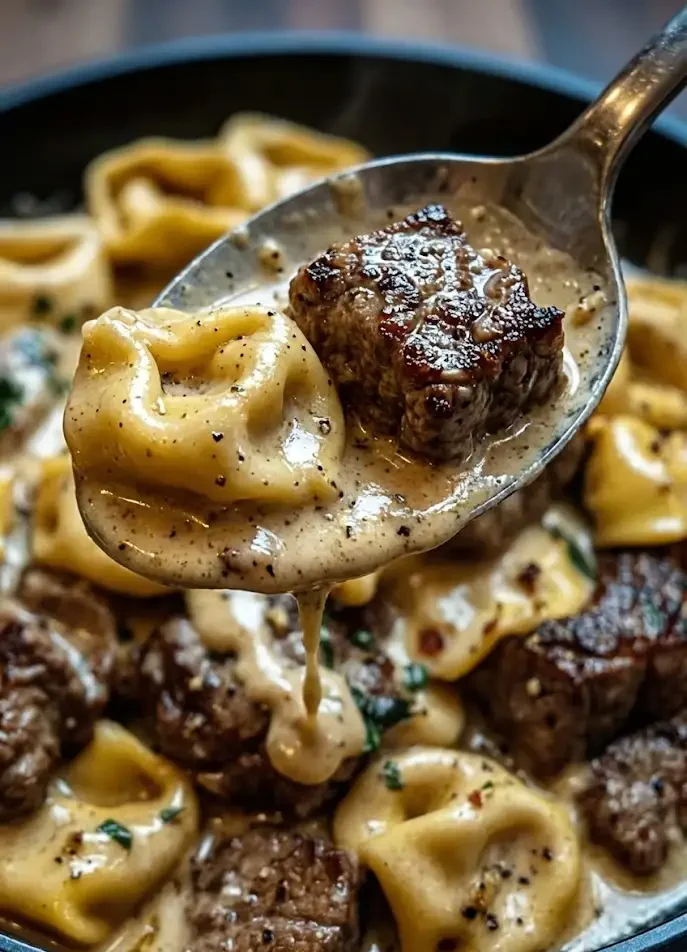 Spoon lifting cracked garlic steak and cheese tortellini coated in creamy Creamhouse sauce, close-up view
