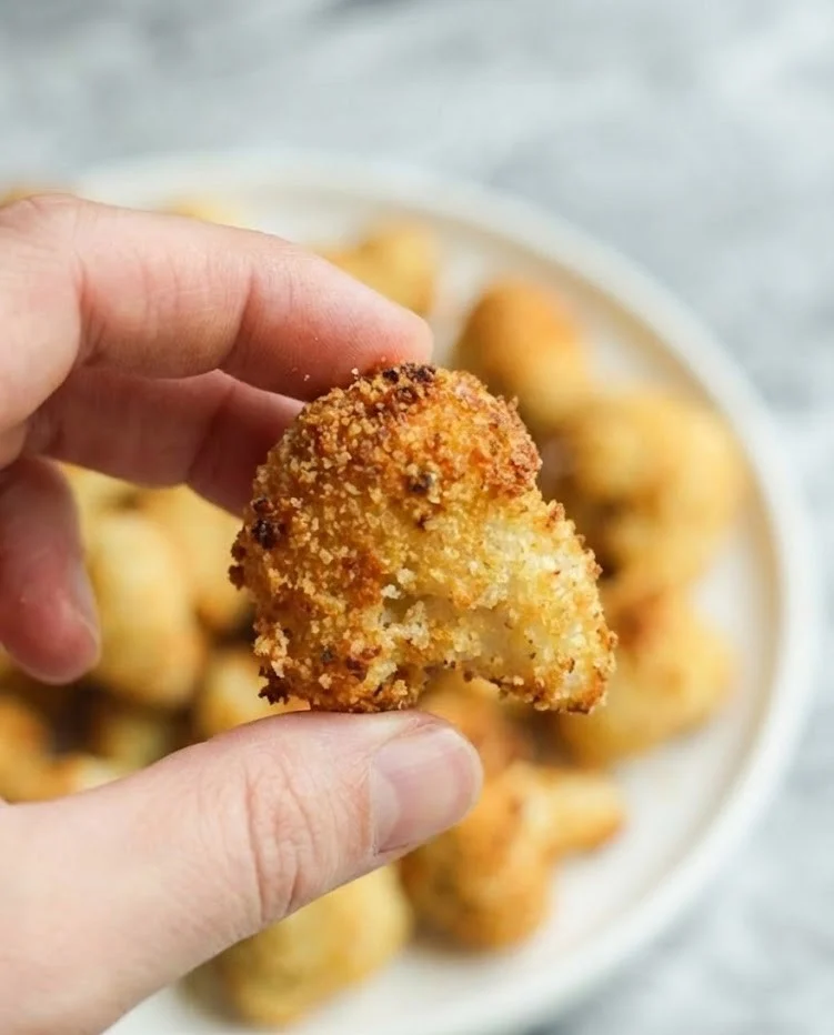 Hand holding a crispy cauliflower bite with golden crunchy coating close up