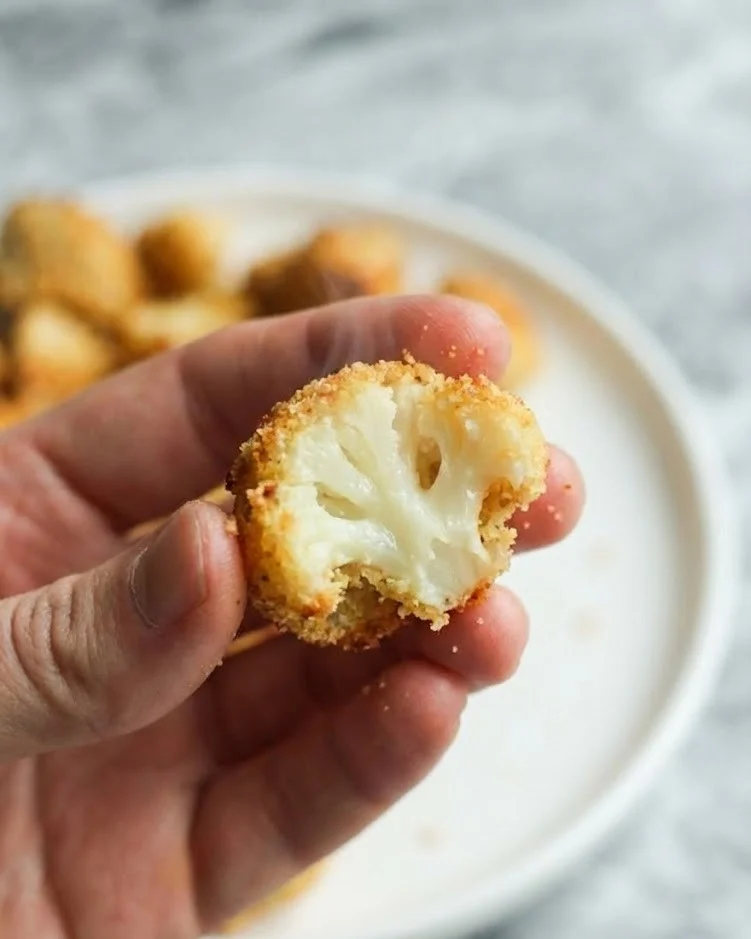 Hand holding a crispy cauliflower bite showing the tender white cauliflower inside with crunchy coating