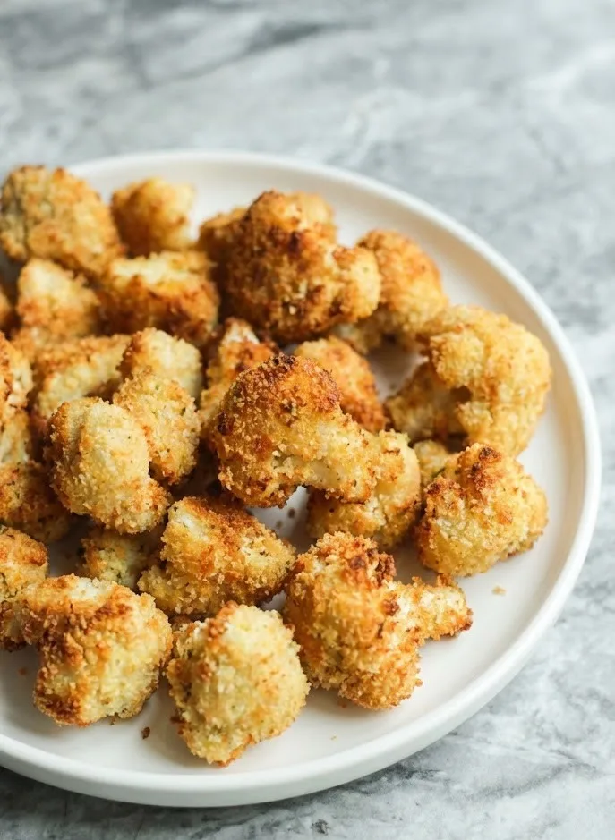 Close up of crispy cauliflower bites with golden crunchy breadcrumb coating on a plate