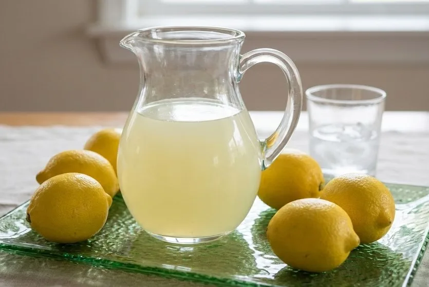 Pitcher of homemade ginger lemonade surrounded by fresh whole lemons