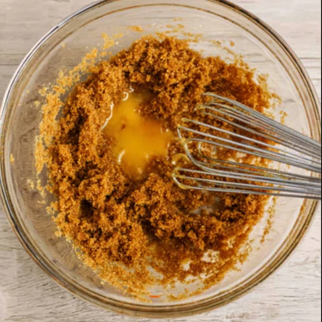 Mixing wet ingredients for gingerbread cookies with molasses, butter, and brown sugar in a bowl