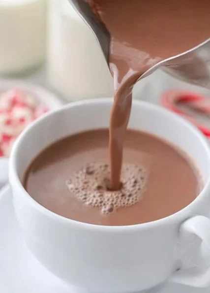 Pouring homemade hot chocolate into a white mug on a saucer