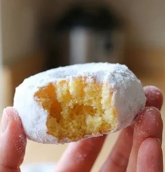 Snowball donut with a bite taken out showing soft fluffy inside and powdered sugar coating