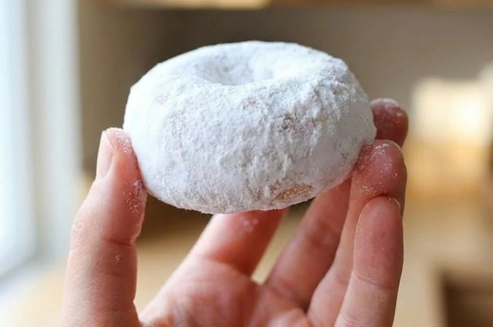 Snowball donut coated in powdered sugar held in hand showing soft texture