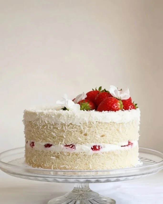 Strawberry coconut sponge cake layered with fresh strawberries and coconut on a glass cake stand