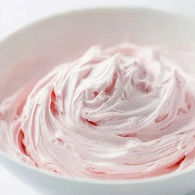 Fluffy strawberry marshmallow frosting with light pink swirls in a white bowl