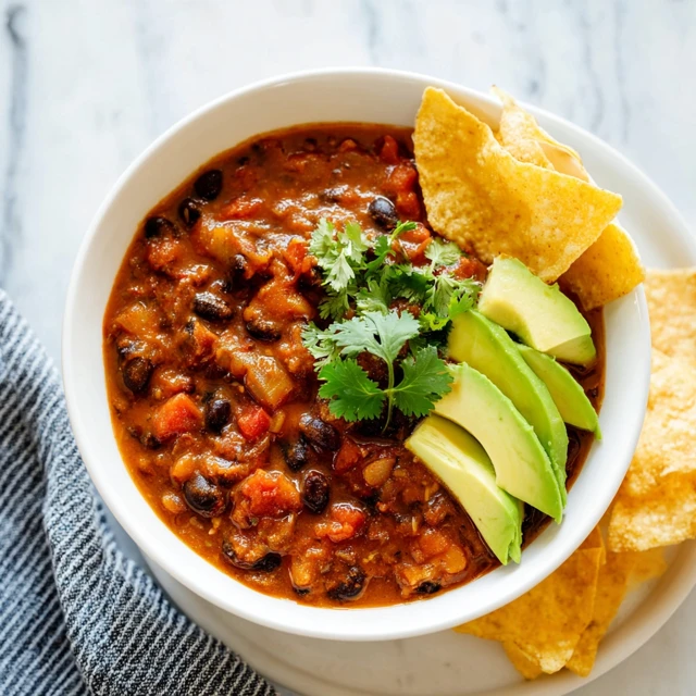 Homemade vegetarian chili with black beans and vegetables served with avocado slices, cilantro, and tortilla chips