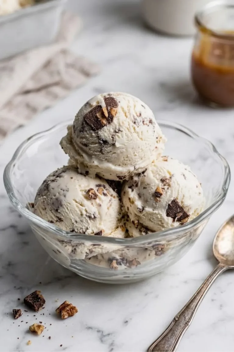 Three scoops of creamy Browned Butter Pecan Ice Cream served in a glass bowl on a marble surface with pecans nearby.