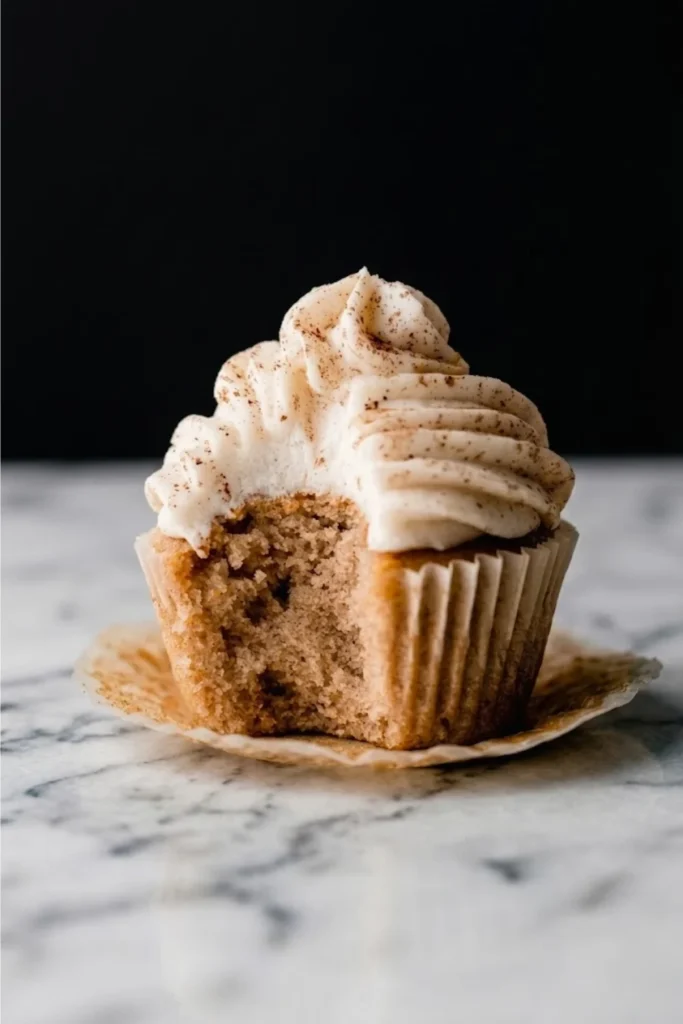 A delicious cupcake with thick Chai Spice Buttercream frosting sitting on a marble countertop with a paper liner.