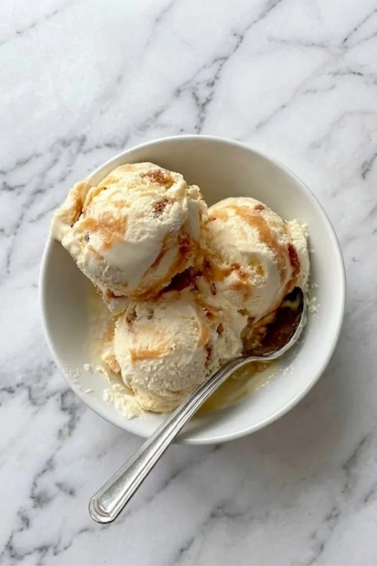Overhead view of three scoops of honeycomb ice cream in a white bowl showing caramel ripples and crunch.