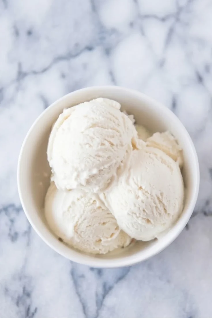 Close-up of three scoops of smooth, creamy vanilla ice cream in a white ceramic bowl.