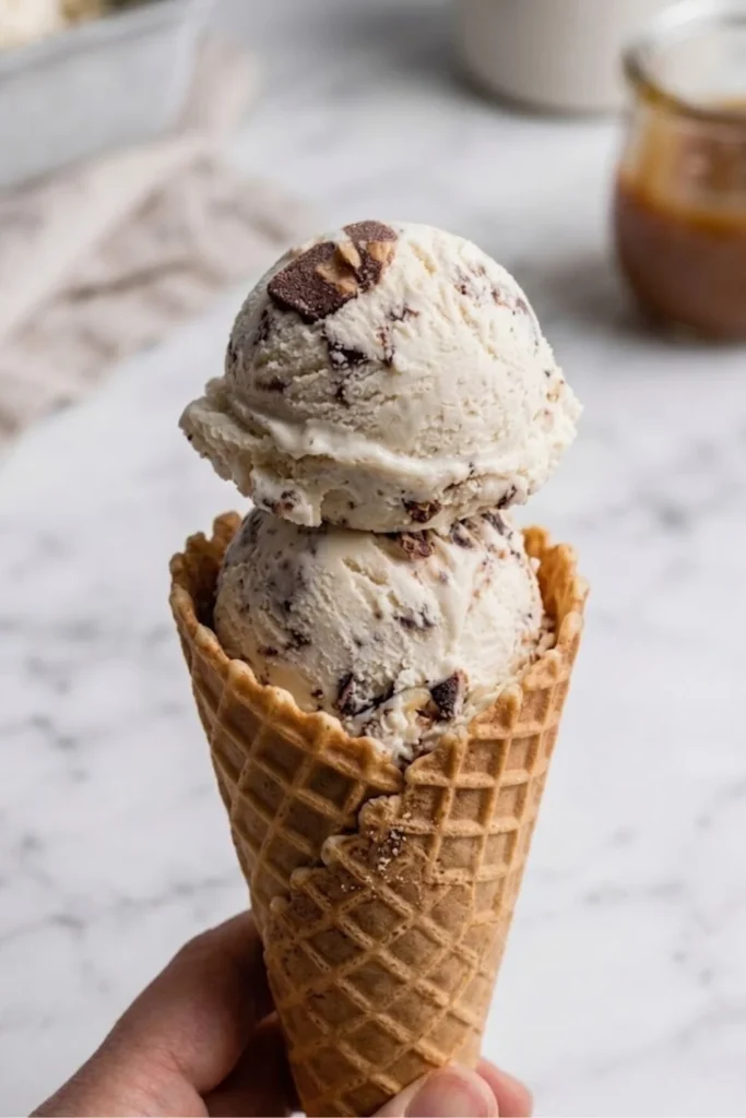 A hand holding a crispy waffle cone topped with two generous scoops of Browned Butter Pecan Ice Cream.