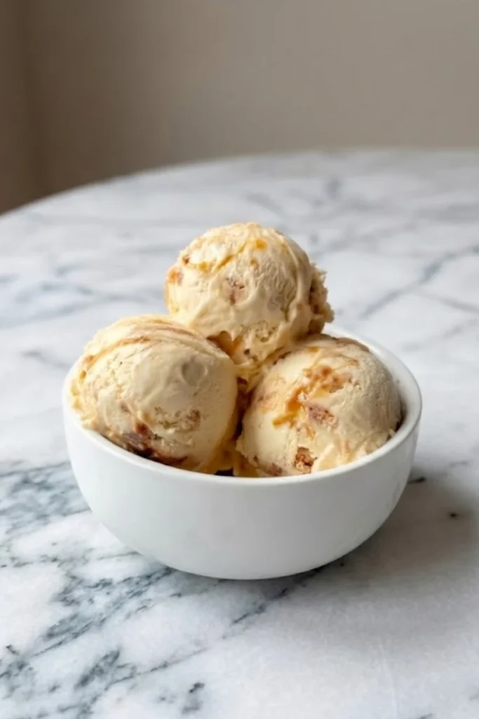Three perfect scoops of homemade honeycomb ice cream served in a clean white bowl on a marble counter.