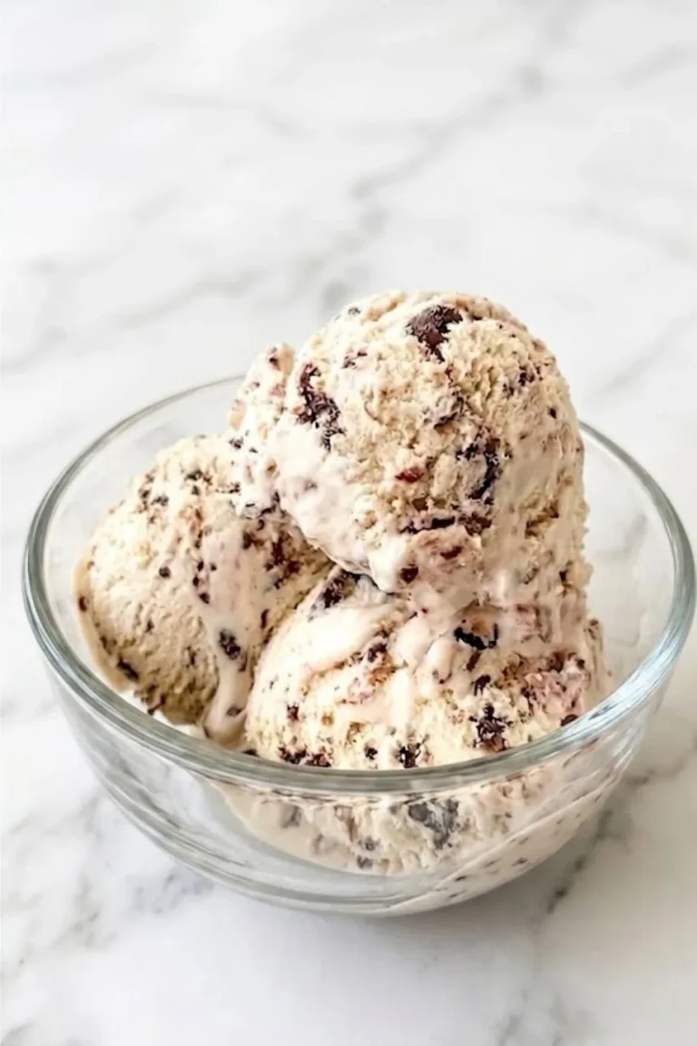 A close-up view of three scoops of creamy homemade No-Churn Chocolate Chip Ice Cream in a clear glass bowl on a marble counter.