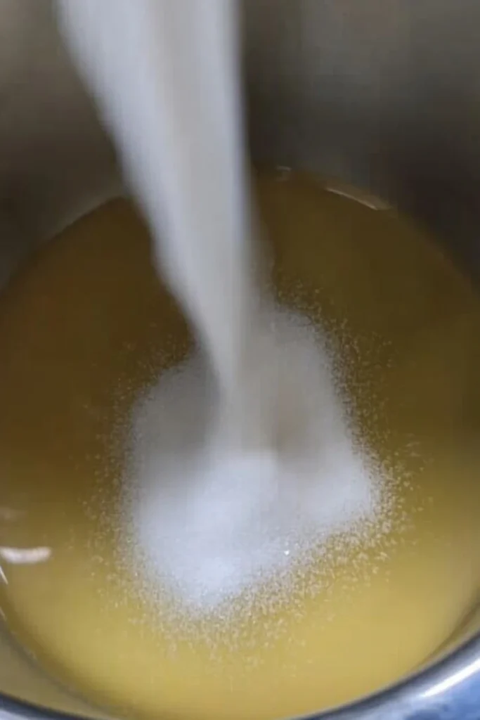 Pouring white granulated sugar into a saucepan with golden syrup for homemade honeycomb ice cream.