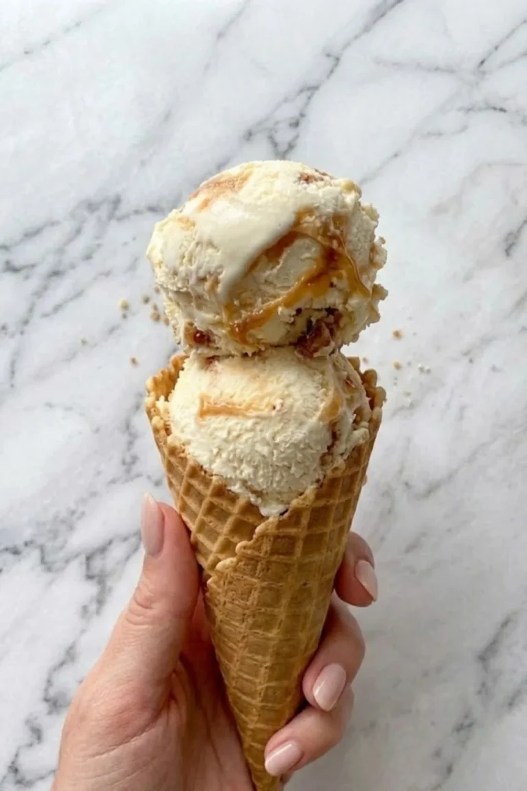 A hand holding a crispy waffle cone topped with two generous scoops of creamy honeycomb ice cream.
