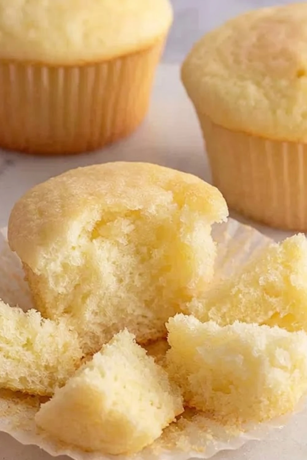 A close-up of a fluffy vanilla cup cake broken open to show the moist and tender crumb texture.
