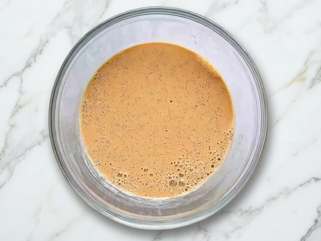 A top-down view of a glass bowl containing the liquid pumpkin and spice base for no-churn ice cream.