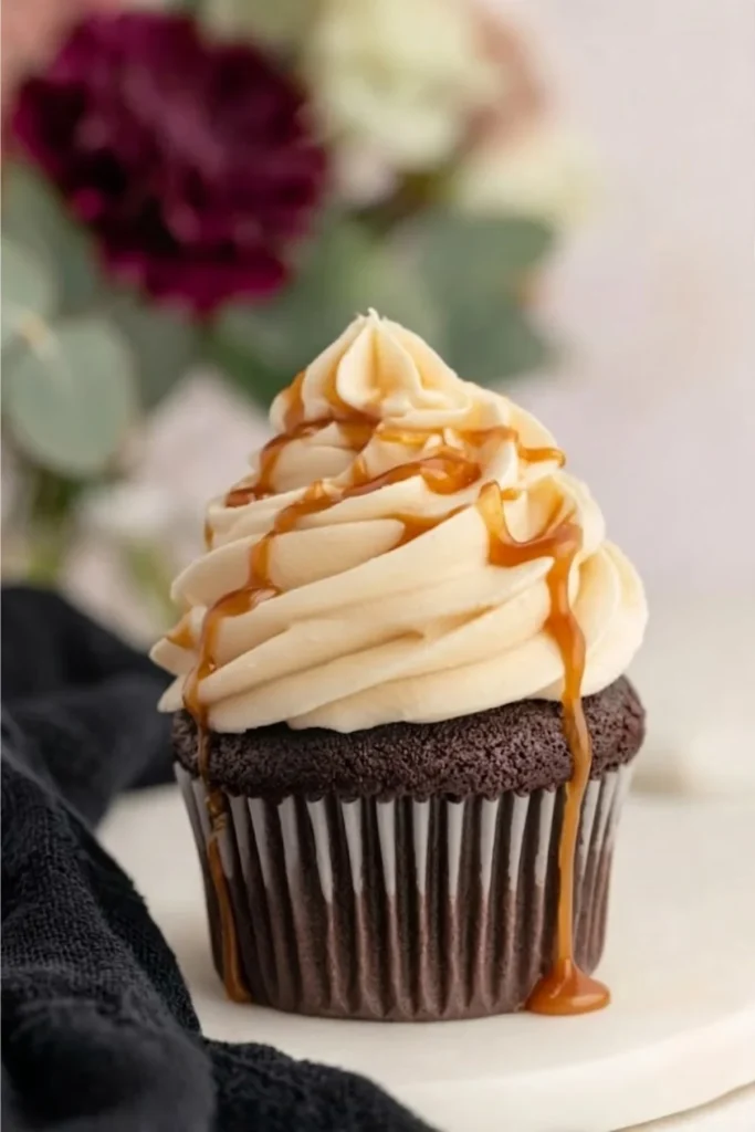 A perfect dark chocolate cupcake with a tall swirl of salted caramel frosting and caramel sauce dripping down the sides.