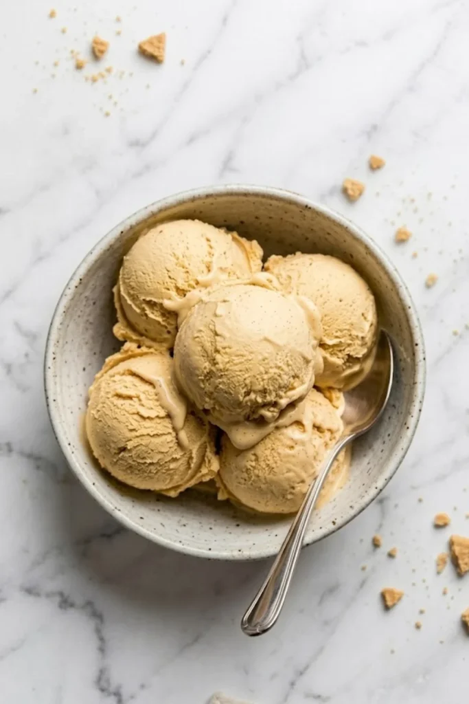 A beautiful bowl of No-Churn Pumpkin Ice Cream scoops served on a white marble surface with cookie crumbles.