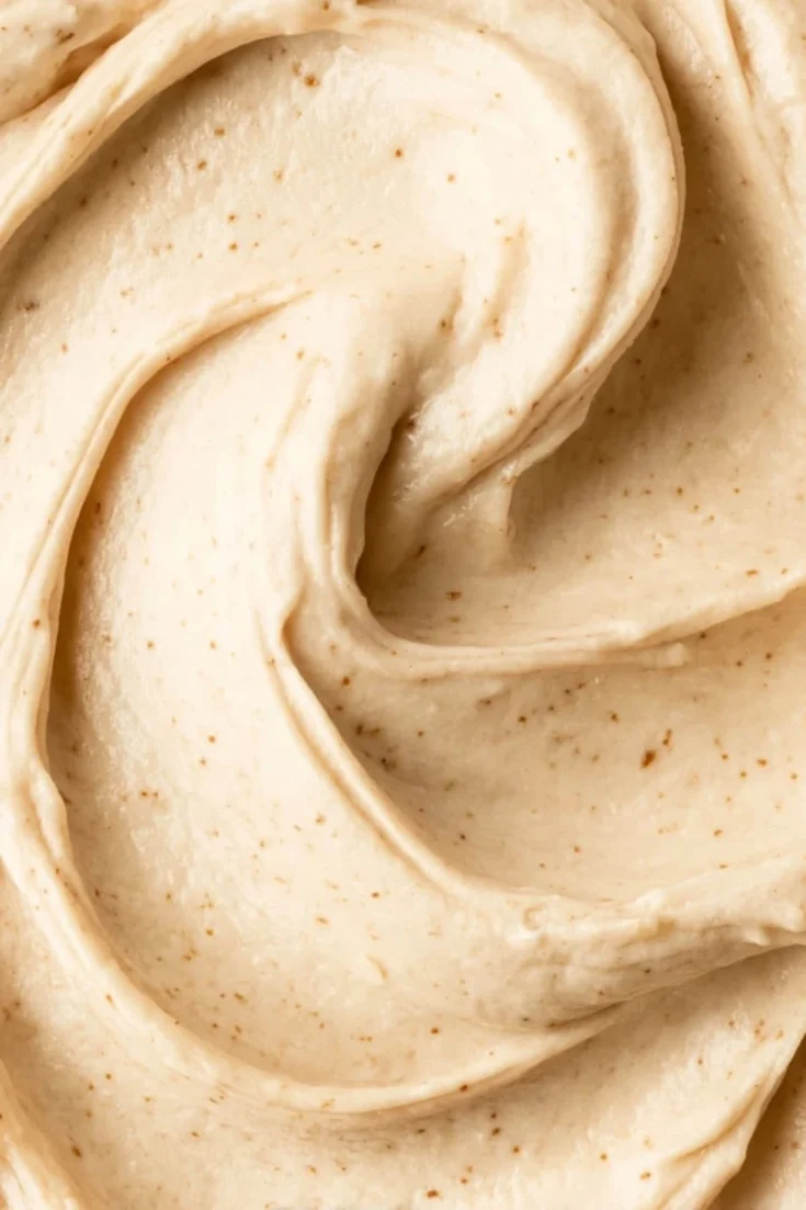 Extreme close-up of the smooth and silky texture of salted caramel frosting showing tiny specks of sea salt and caramel.