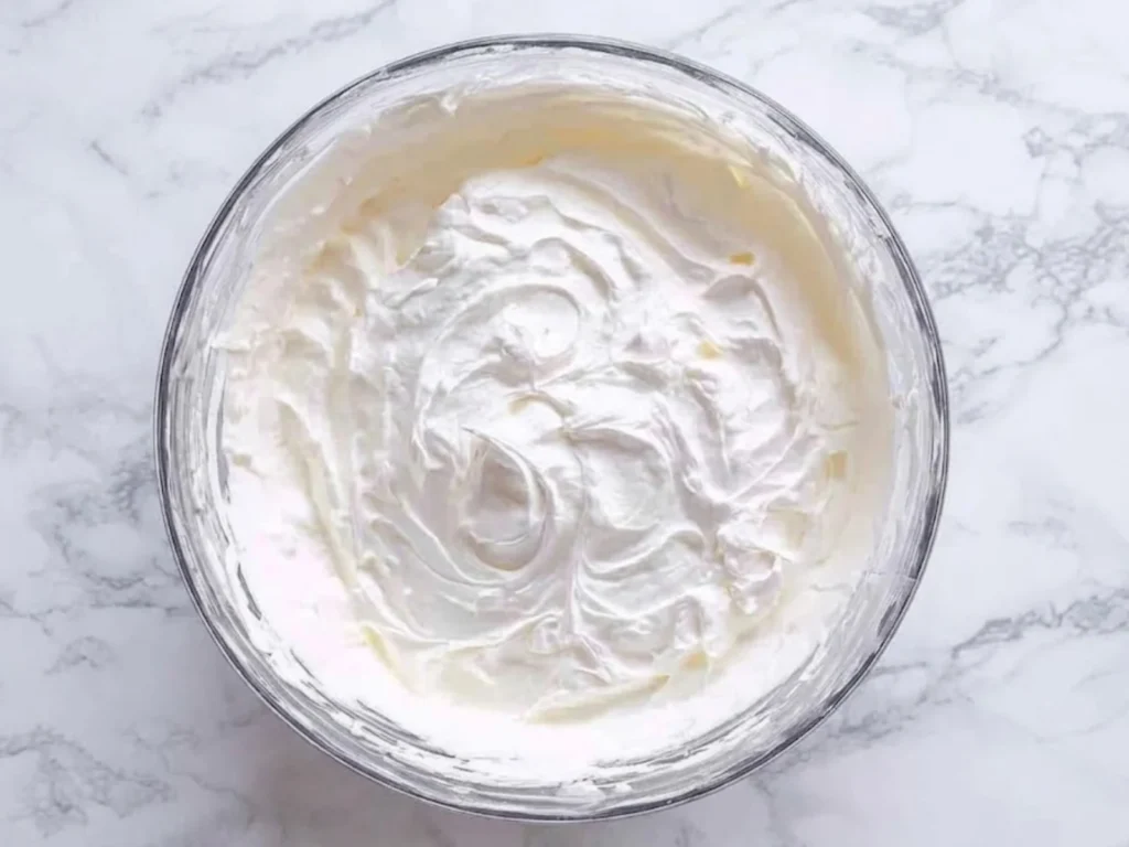 A glass bowl of heavy whipping cream beaten into stiff peaks for a no-churn ice cream base.