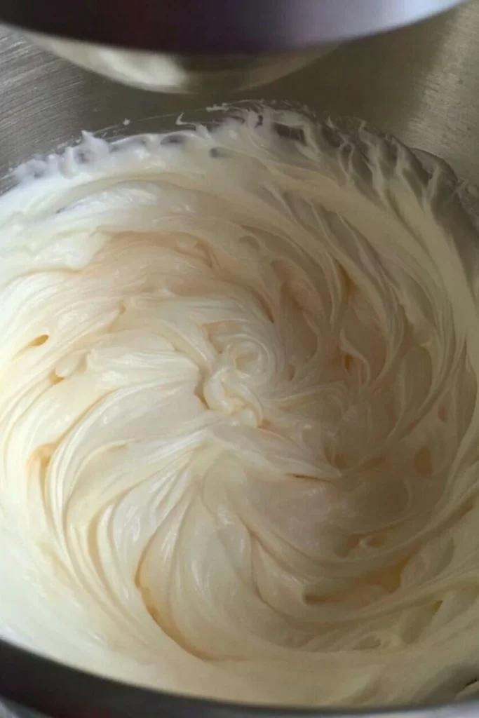 Fluffy stiff peaks of whipped heavy cream in a metal mixing bowl for a no-churn ice cream base.